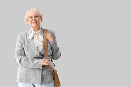 Senior businesswoman in eyeglasses with bag on light backgroundの写真素材