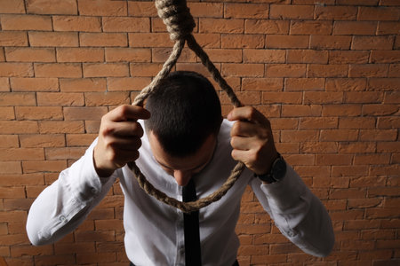 Businessman going to hang himself on brick background. International Stress Awareness Weekの写真素材