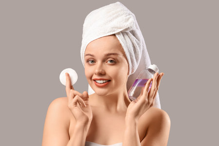 Young woman with bottle of micellar water and cotton pad after shower on gray background, closeupの写真素材