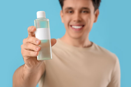 Young man with bottle of micellar water on blue background, closeupの写真素材