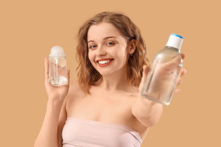 Young woman with bottles of micellar water on beige backgroundの写真素材