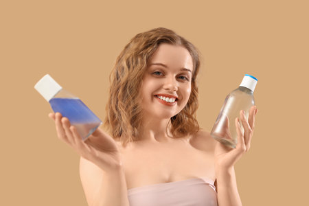 Young woman with bottles of micellar water on beige backgroundの写真素材
