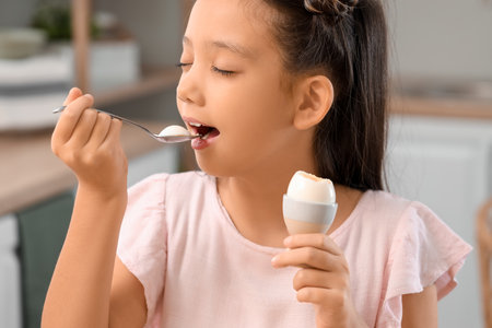 Cute Asian girl eating boiled egg in kitchen, closeupの写真素材