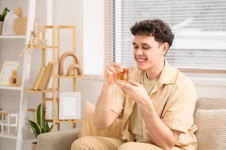 Young man with Turkish tea sitting on sofa at homeの写真素材