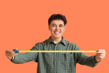Young man with tape measure on orange background