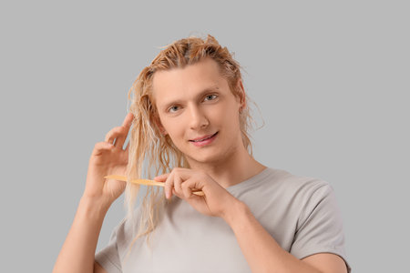 Young blonde man combing wet hair on light backgroundの写真素材