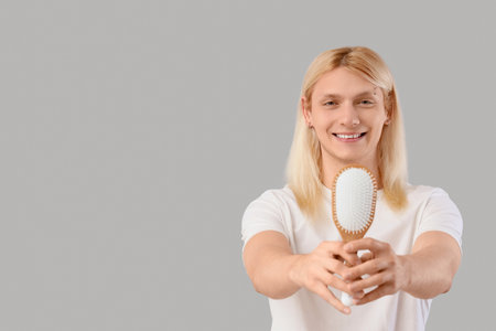 Young blonde man with brush on light backgroundの写真素材