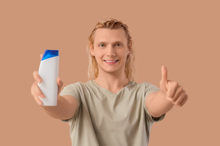 Young blonde man with shampoo showing thumb-up on beige backgroundの写真素材