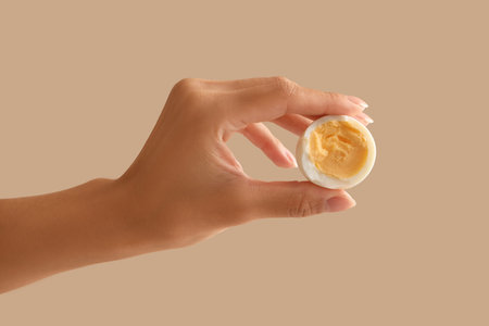 Female hand with boiled egg on beige background