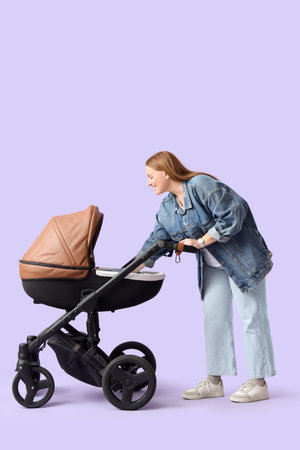 Young mother with baby stroller on lilac background
