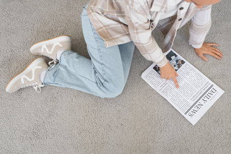 Young woman with newspaper on carpet at home, top viewの写真素材