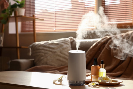 Aroma diffuser with plumeria flowers and essential oils on table in living room