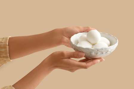 Female hands with bowl of boiled eggs on beige backgroundの写真素材