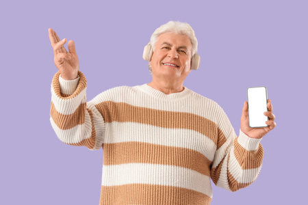 Senior man in headphones with mobile phone listening to radio on lilac backgroundの写真素材