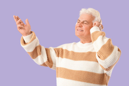 Senior man in headphones listening to radio on lilac backgroundの写真素材