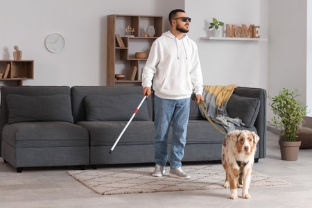Blind young man with stick and guide dog walking at homeの写真素材