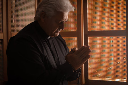 Senior priest with beads praying in confession boothの写真素材