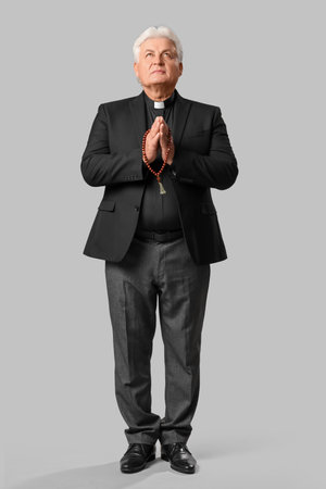 Senior priest praying with beads on gray backgroundの写真素材