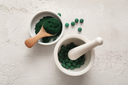 Bowl of spirulina powder with spoon, mortar and tablets on light grunge backgroundの写真素材