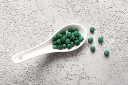 Spoon with spirulina tablets on gray grunge backgroundの写真素材