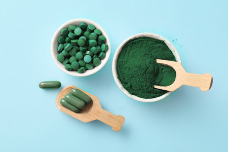 Bowls of spirulina tablets and powder with wooden scoops on blue backgroundの写真素材