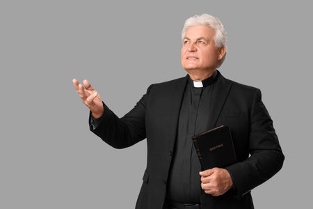 Senior priest with Bible on gray background