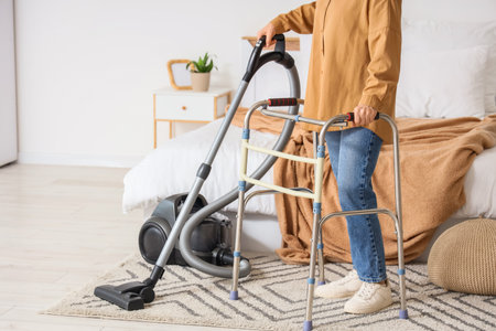 Mature woman with walker vacuum cleaning carpet in bedroomの写真素材
