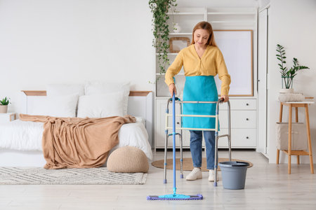 Mature woman with walker mopping floor in bedroomの写真素材
