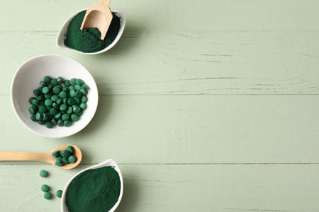 Bowls of spirulina powder and tablets with scoop on green wooden backgroundの写真素材