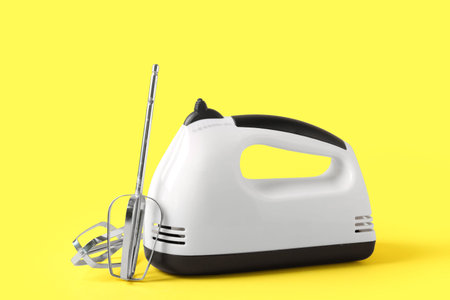 Electric mixer with chrome beaters on yellow background