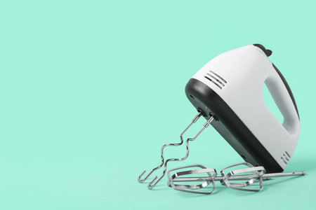 Electric mixer with chrome beaters on turquoise background