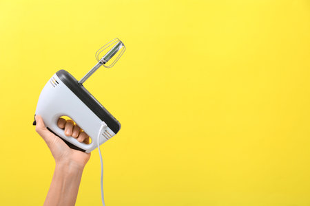 Woman holding electric mixer on yellow background