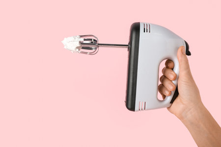 Female hand with electric mixer and whipped cream on pink backgroundの写真素材