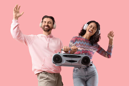 Young couple in headphones with boombox dancing on pink background