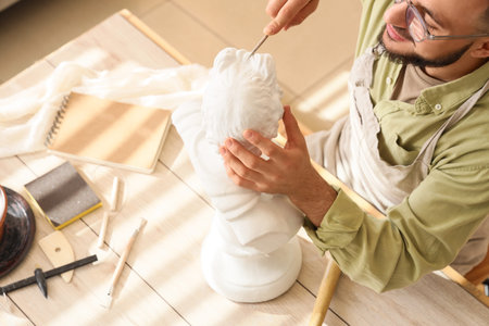 Male sculptor working with bust at table in workshop, top viewの写真素材