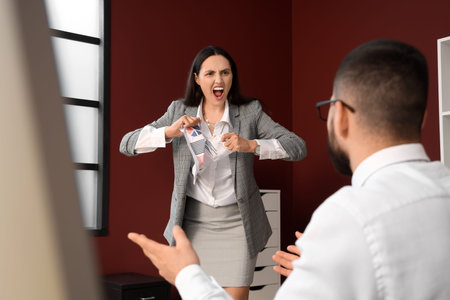 Angry female boss tearing document with her employee in office