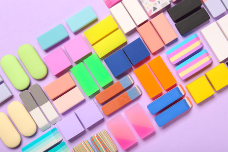 Different colorful rubber erasers on purple background