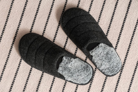 pair of black fuzzy slippers on striped beige carpet