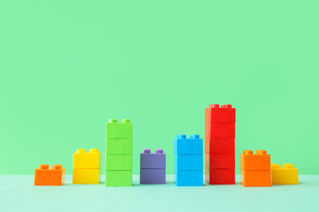 Colorful plastic building blocks arranged as bar graph on green background, education and business growth