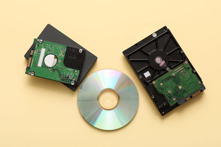 Different hard drives and CD disk on beige background