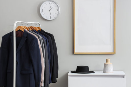Rack with different stylish male suits and chest of drawers in dressing room