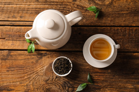 White ceramic teapot with a cup of hot green tea and loose tea leaves on a rustic wooden table, a small bowl of loose green tea leaves and fresh tea sprigs complement the setting