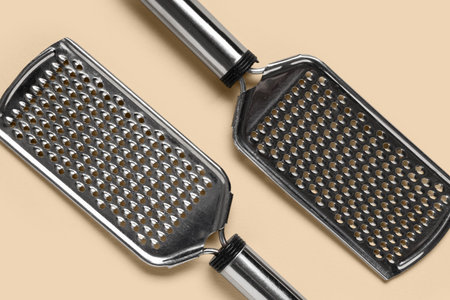 Kitchen utensil and cooking equipment, two metal graters for food preparation on a light beige background