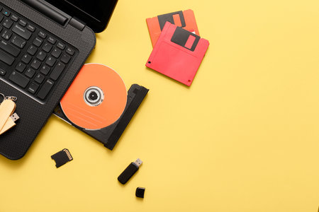 Laptop with CD disk and different memory storage devices on yellow background