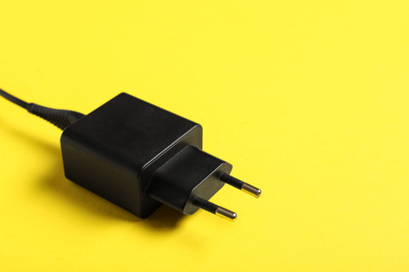Modern power adapter with USB cable on yellow background, closeup