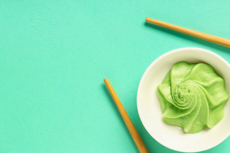 Bowl with wasabi paste and chopsticks on turquoise background