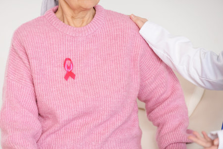 Senior woman with pink ribbon visiting doctor in clinic, closeup. Breast cancer awareness concept