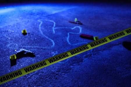 Crime scene investigation and forensic evidence, chalk outline with police warning tape and handgun on dark ground at night