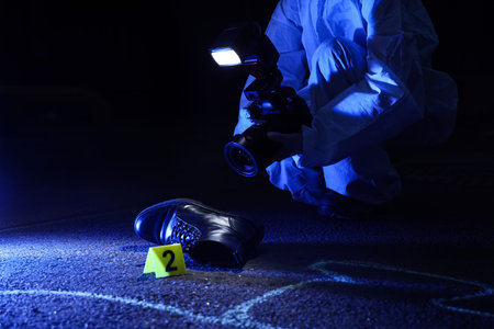 Forensic investigation and crime scene analysis, criminalist documenting evidence with camera and marker at night in dark urban environment