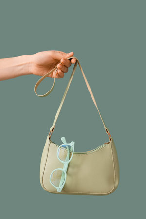 Female hand with handbag and eyeglasses on mint background